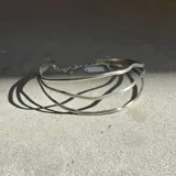 Gargantilla rígida de diseño triple con estructura ondulada en metal dorado, que se completa con una cadena fina ajustable en la parte posterior.