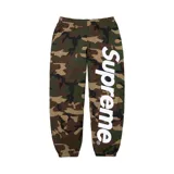 Pantalón de jogging Supreme con estampado de camuflaje woodland y logo de la marca estampado en tipografía grande y vertical en color blanco sobre la pierna izquierda.