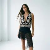 Chaleco negro de terciopelo con bordados florales en blanco y plateado, escote en V pronunciado y ribete plateado.