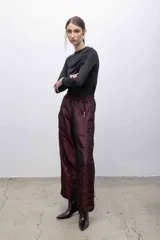 Pantalón de tafeta tornasolada color borgoña, de corte recto y tiro alto, con cintura elastizada, bolsillos frontales con cierre y cordones ajustables en las pantorrillas para fruncir el bajo.