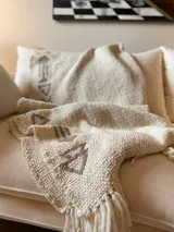 Manta de lana color crudo con bordados de flechas en color marrón.