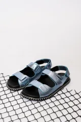 Sandalias chatas con base negra y tiras anchas de cuero sintético color celeste metalizado.