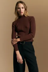 Polera de tejido acanalado con cuello alto, corte ajustado al cuerpo y mangas tres cuartos con terminaciones onduladas en los puños.