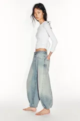 Jeans de mezclilla de tiro medio con diseño amplio tipo balloon, costuras marcadas y bajo con puño elástico. Cuenta con bolsillos delanteros y traseros, y cierre frontal con cremallera y botón metálico.