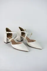 Sandalia de tacón cuadrado color blanco, con diseño de punta fina cerrada y tiras cruzadas ajustables con hebillas metálicas doradas.