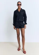 Chaqueta de denim azul oscuro con cuello solapa, cierre frontal de botones y dos bolsillos de parche en el pecho.
