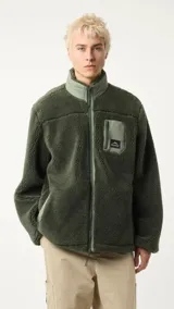Campera de polar verde militar con cierre frontal y cuello alto. Tiene un bolsillo con cierre en el pecho y dos bolsillos laterales.