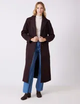 Tapado largo de bouclé color marrón oscuro, con silueta entallada que termina en evasé. Tiene cuello de solapa amplia, cierre frontal con tres botones a tono y bolsillos funcionales con solapa. Incluye forro interno a tono.