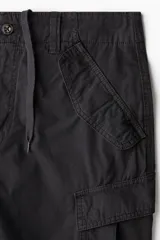 Pantalón cargo de corte holgado en color negro, con múltiples bolsillos laterales con solapa, pliegues en las rodillas y cordones ajustables en el bajo.