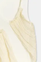 Top de cuello redondo y sin mangas, confeccionado en tejido de punto acanalado color crema. Presenta una aplicación asimétrica de tela tipo georgette en tono beige claro que cruza el frente de la prenda.