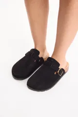 Zuecos negros con capellada cerrada, tira con hebilla metálica regulable en el empeine, y base de corcho con suela de goma.
