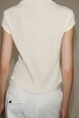 Camiseta de canalé color blanco, de corte slim fit, cuello redondo, manga corta y cierre frontal con hilera de botones oscuros a contraste.