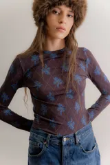 Remera de manga larga confeccionada en algodón elastizado, con cuello redondo y diseño ajustado al cuerpo. Presenta un estampado de rombos finos con motivos florales en tonos azules sobre una base de color marrón oscuro.