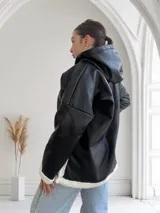 Buzo negro de ecocuero con capucha, cierre dorado a mitad del torso y puños y ruedo con forro de piel sintética blanca.