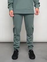 Pantalón cargo de hombre color verde musgo, confeccionado en mezcla de algodón, poliéster y elastano. Presenta bolsillos cargo en los muslos y puños ajustados en los tobillos.