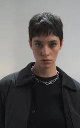 Campera tipo sobrecamisa de diseño oversize, confeccionada en microfibra opaca con patrón matelaseado geométrico. Presenta cuello, puños, cartera central y ruedo en gabardina de algodón, con cierre frontal mediante broches a presión. El diseño del ruedo simula una prenda superpuesta.