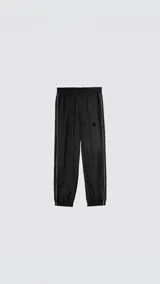 Pantalón deportivo de microfibra opaca, color negro, con diseño de vivos laterales blancos a contratono. Presenta cintura elástica y puños elásticos en los tobillos, con un pequeño logo bordado en la parte superior.