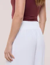 Pantalón negro de calce relajado y caída fluida, confeccionado en poliéster con textura de crepé. Tiene cintura alta elastizada estilo pull on con un aplique de cadena metálica decorativa, y pierna de corte ancho tipo wide leg corto por arriba del tobillo.