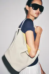 Bolso de hombro de piel en color blanco, con diseño tipo bucket, asa fija y detalle de tira colgante con nudo en el lateral.