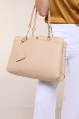 Cartera de hombro de cuero sintético beige, con estructura tripartita de compartimento central con cierre y dos compartimentos laterales con broche magnético. Posee asas dobles con detalles de cadena metálica dorada y un tarjetero independiente desmontable.