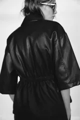 Chaqueta efecto piel color marrón, con cuello solapa, mangas por debajo del codo, cintura elástica, falsos bolsillos delanteros y cierre frontal con cremallera.