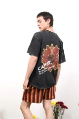 Remera negra de algodón con efecto acid wash, con estampado de girasol en la espalda y la palabra "CAPER." en blanco.