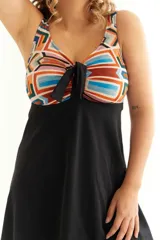 Malla entera con short y vestido negro, con corpiño estampado con motivos geométricos en tonos naranja, celeste y marrón. Presenta un nudo en el centro del escote para regular la profundidad.