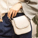 Mini cartera bandolera de cuero, de formato compacto y diseño atemporal con solapa frontal y costuras artesanales decorativas en el borde. Cuenta con el logotipo de la marca grabado en la parte delantera y correa larga regulable.