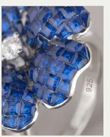 Anillo de plata 925 con diseño de flor, decorado con incrustaciones de piedras azules y un centro brillante.