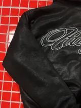 Campera de cuero sintético negro con diseño tipo bomber, cuello camisero y puños y ruedo elásticos. Presenta un bordado grande en la espalda con tipografía cursiva en color blanco.
