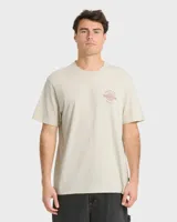 Remera Billabong de manga corta y corte regular, color beige, con gran estampado gráfico en la espalda que incluye el texto "Billabong", la ilustración de una quilla de tabla de surf y un sol estilizado.