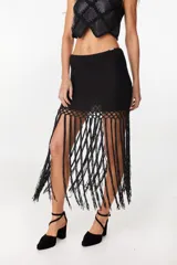 Falda corta negra de tejido de punto con detalle de crochet en la parte inferior y largas tiras colgantes a modo de flecos.