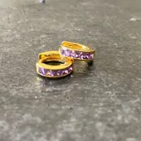 Par de aros tipo argolla pequeños, dorados, con hilera de circonias color púrpura. Cierre a presión.