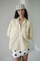 Camisa de manga larga color amarillo claro, con cuello clásico, botonadura frontal y doble bolsillo delantero. Tiene un calce relajado y terminación curva en el ruedo.