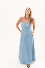 Vestido largo de denim fino y liviano, color celeste, con breteles finos, escote delicado, silueta entallada en la parte superior, falda amplia con recortes verticales y bolsillos laterales.