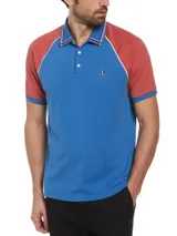 Chomba de hombre con mangas cortas raglán, color azul con mangas color ladrillo y detalles en blanco. Confeccionada en tejido interlock de algodón orgánico y logo bordado en el pecho.