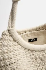 Bolso tipo shopper color crudo, confeccionado en tejido trenzado de algodón con diseño de macramé. Cuenta con dos asas de hombro ajustables que funcionan como cierre del compartimento principal.