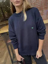 Buzo de punto color azul marino con diseño de conejos bordados a mano en la espalda en tonos rojizos y detalles de puntos verdes en el ruedo. Presenta cuello redondo y mangas largas.