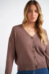 Cárdigan de tejido liviano con textura acanalada, cuello en V y cierre frontal con botones. Presenta mangas largas y un diseño clásico con detalle de grifa en cuero.