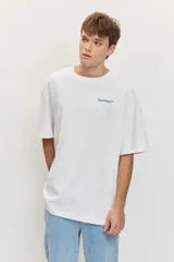 Remera blanca de manga corta, corte oversize, con estampa en la espalda de una flor sobre fondo difuminado verde y blanco.