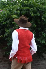 Chaleco de punto tejido a mano con lana merino, color blanco, con cuello redondo, detalles de flecos en el ruedo y aplique de etiqueta de cuero con la marca.