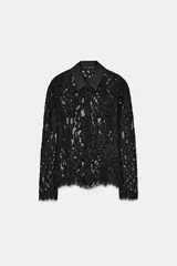 Camisa de manga larga confeccionada en encaje negro con patrón floral. Presenta cuello solapa de tejido liso negro y cierre frontal de botones. El bajo del ruedo y los puños tienen terminación de encaje festoneado.