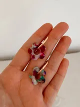 Aros tipo argolla con dije colgante en forma de flor realizado en acrílico con acabado brillante y destellos iridiscentes.