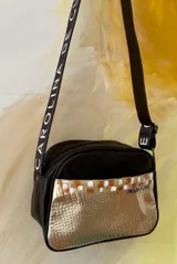 Bandolera Kaira de la línea Ottenta de Carolina de Cunto, color negro con bolsillo frontal dorado texturizado de efecto reptil y arte pintado a mano. Cuenta con correa regulable negra con el logo de la marca en blanco.