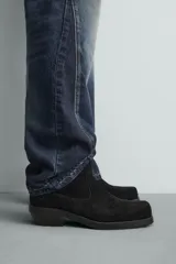 Bota estilo cowboy de caña media, confeccionada en piel con acabado de serraje. Presenta horma cuadrada, cierre lateral mediante cremallera y suela con tacón bajo.