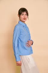 Camisa de manga larga color celeste con rayas verticales blancas, cuello camisero y volados frontales a lo largo de la botonera.