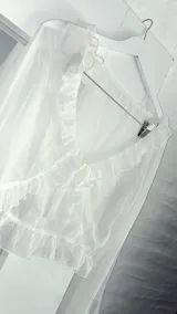 Blusa blanca traslúcida con escote en V, volados en el contorno y mangas largas acampanadas con lazos en los puños.