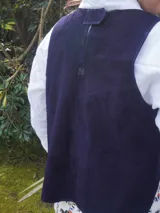 Chaleco de gamuza negro, sin mangas, con cuello redondo y diseño bordado de un sol en el pecho.