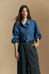 Camisa de jean azul con cuello camisero, mangas largas abullonadas con hombros fruncidos y cierre frontal con botones.