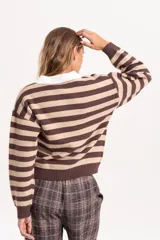 Buzo de punto con diseño a rayas horizontales en tonos marrón y beige. Presenta un cuello polo en color blanco con cierre frontal de botones, mangas largas con puños acanalados y un corte holgado tipo boxy.